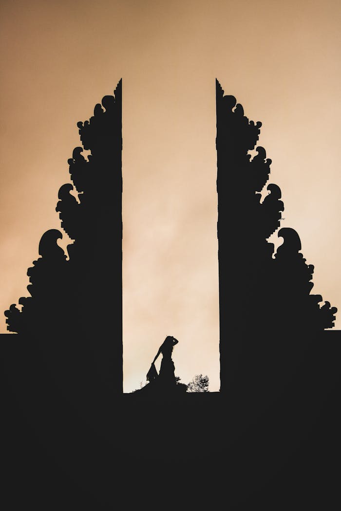 Dramatic silhouette of a person framed by iconic Balinese temple gates at sunset.