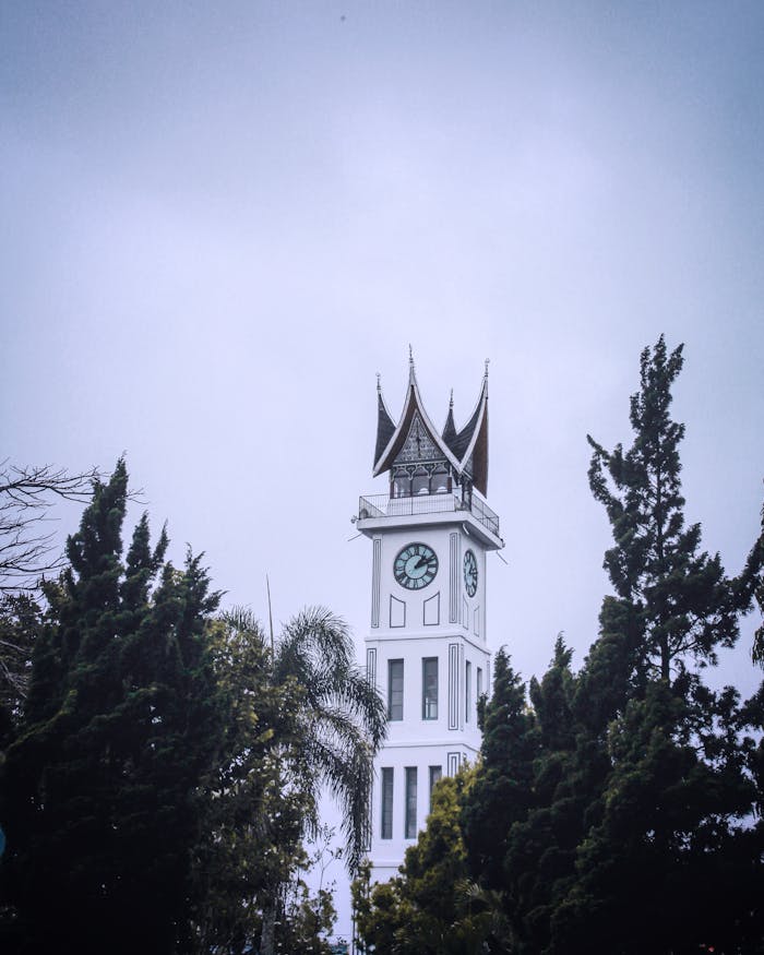 Majestic view of the iconic Jam Gadang clock tower surrounded by trees, under a cloudy sky.
